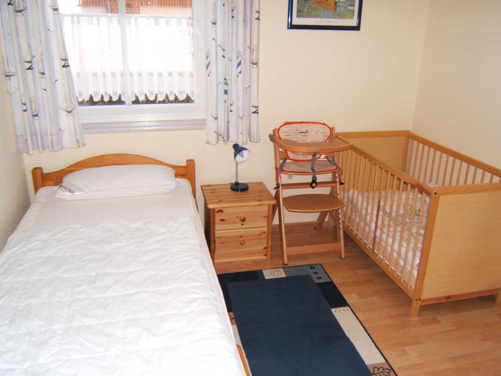 Kinderschlafzimmer: 2 Einzelbette, 1 Kinderbett, Kleiderschrank, Regal mit verschiedenen Kinderbüchern und Spielen